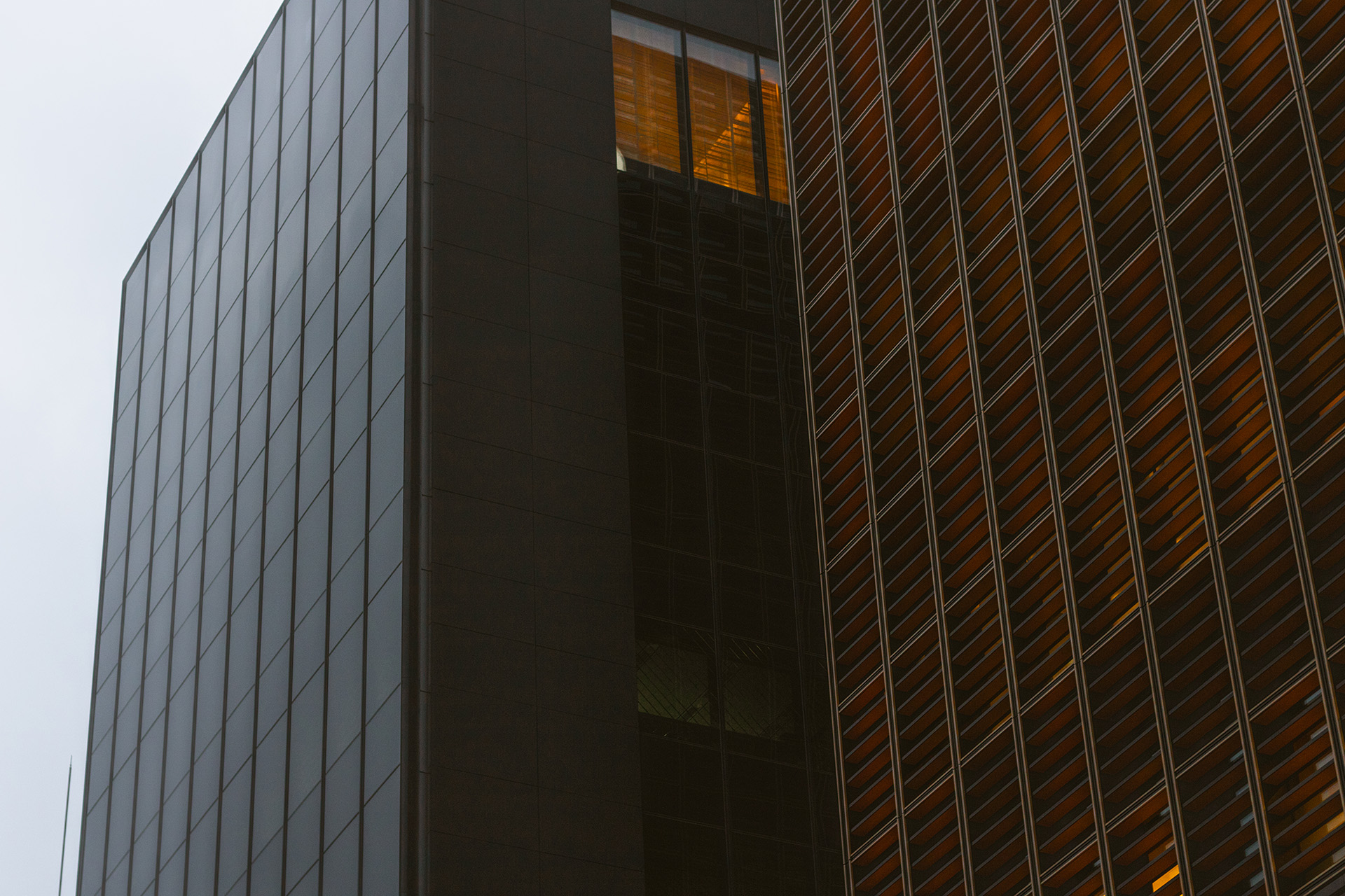 Dark and slick building facade next to another facade with dark orange horizontal struts at its windows.